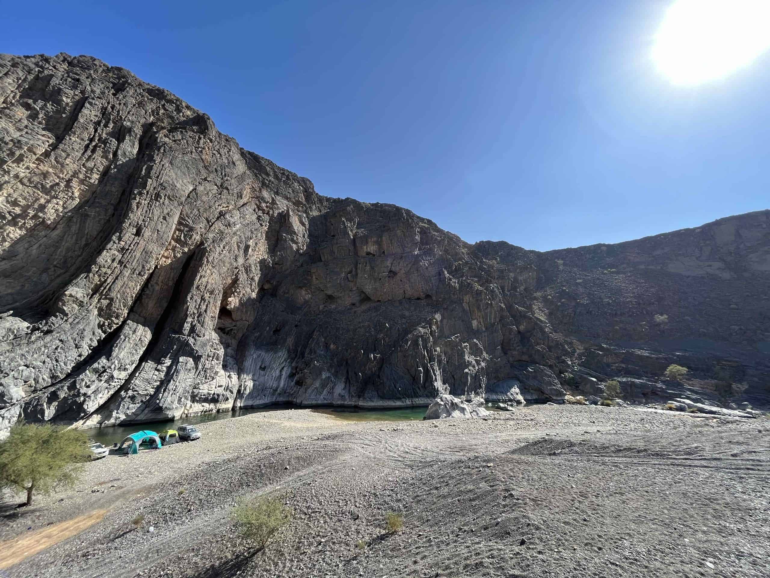 Our camping spot in the valley below Dayqah Dam. A river of clear water flows below a cliff. Our tent is pitched in front of the water