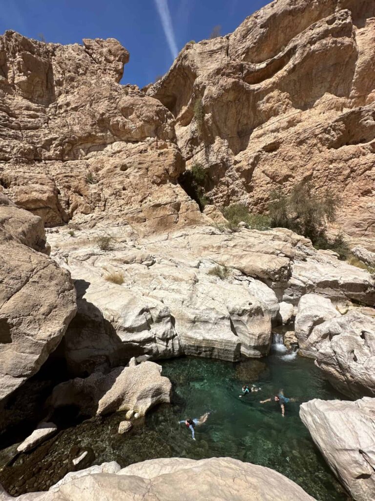 Father and two daughters swim in the clear waters of Wadi Bani Khalid with the rocks walls of the valley rising up behind them