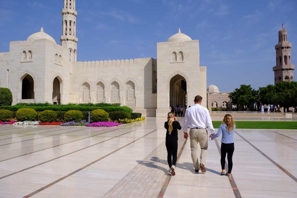 Family walks across marble courtyard of the Sultan Qaboos Grand Mosque in Muscat