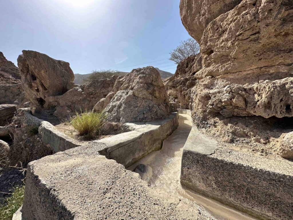 Steaming hot spring water flows through irrigation channel in rocky wadi valley