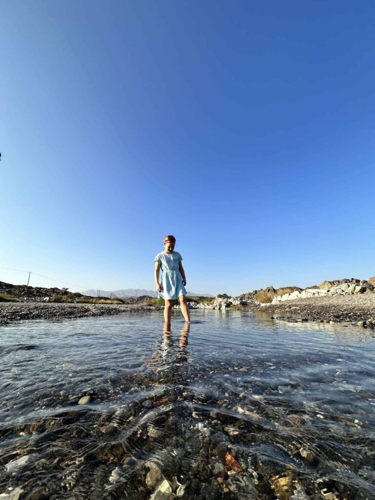 Girl paddling in stream of shallow water flowing over shingle in Wadi Al Khoud