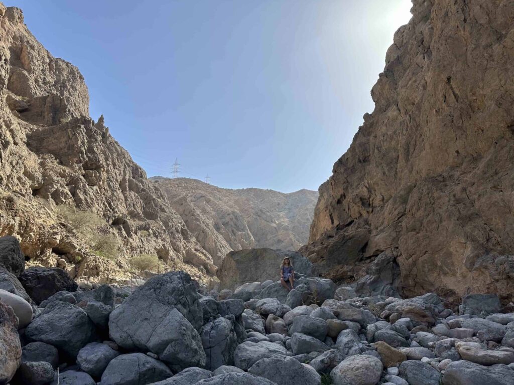 Girl sat on boulder in a rocky valley with cliffs rising on either side