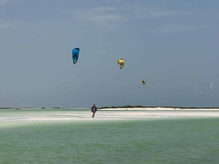 Girl walking across sand bar with kite surfers kites flying in the background
