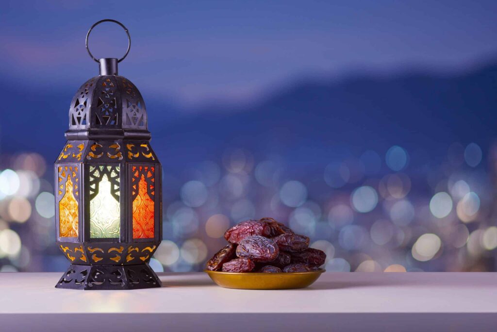 Holy month of Ramadan concept. Righteous Muslim Lifestyle. Ramadan lantern (Fanous), dates.. Mountains and City lights in bokeh blurred background.