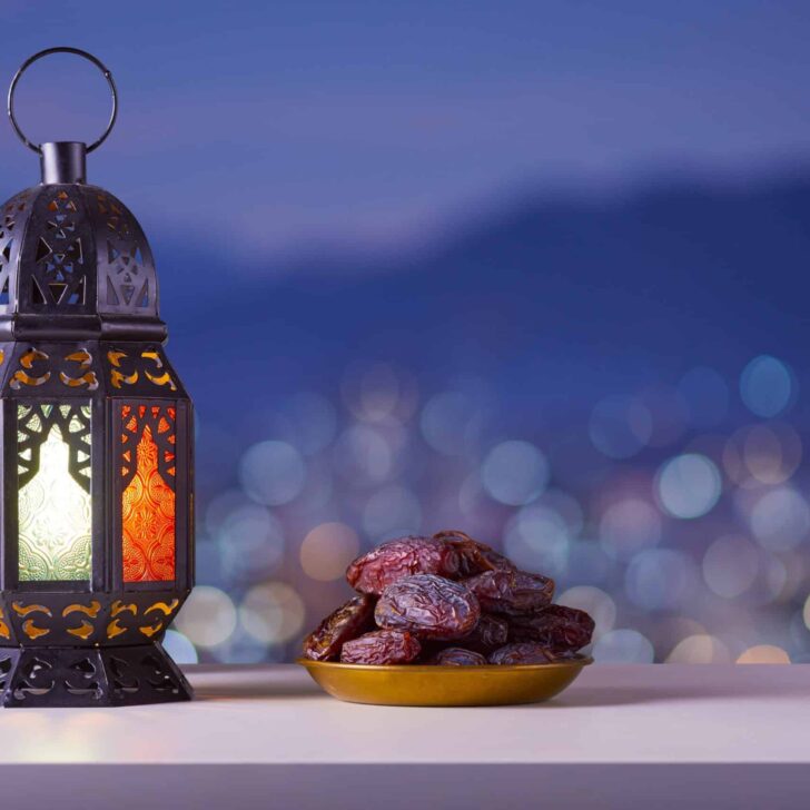 Holy month of Ramadan concept. Righteous Muslim Lifestyle. Ramadan lantern (Fanous), dates.. Mountains and City lights in bokeh blurred background.
