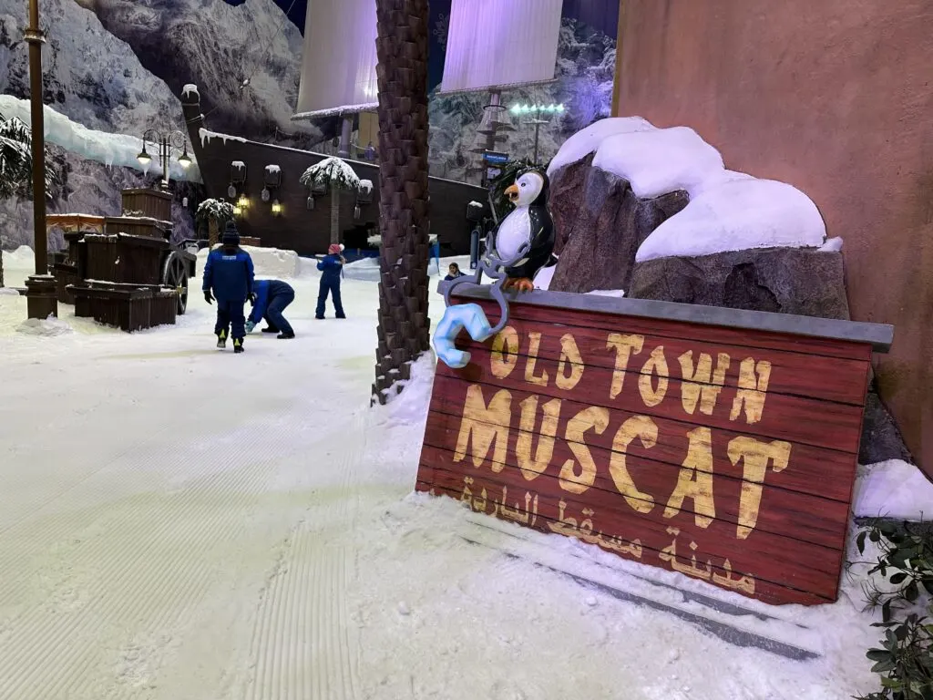 A sign saying Old Town Muscat leant up against a building in the snow