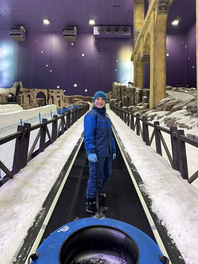 Our daughter wearing a snow suit and woolly hat while pulling a Ringo up a conveyer belt in Snow Oman