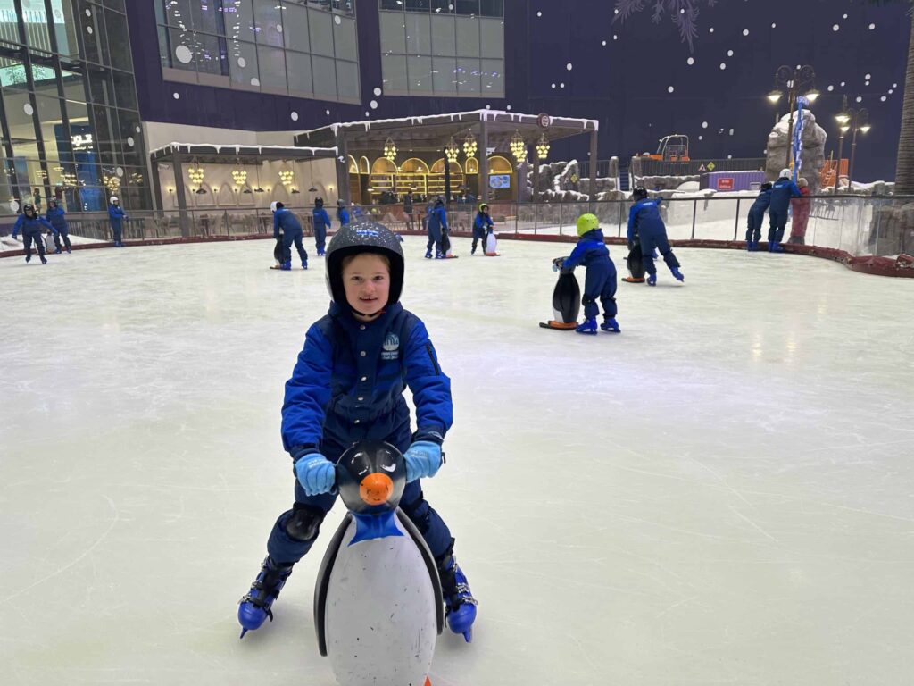 Child in snow suit ice skating with penguin skating aid