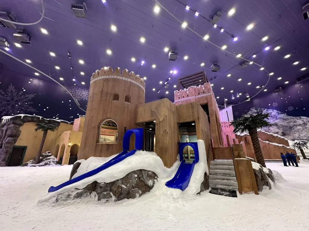 Two children's slides coming out of the side of a mock castle in Snow Oman