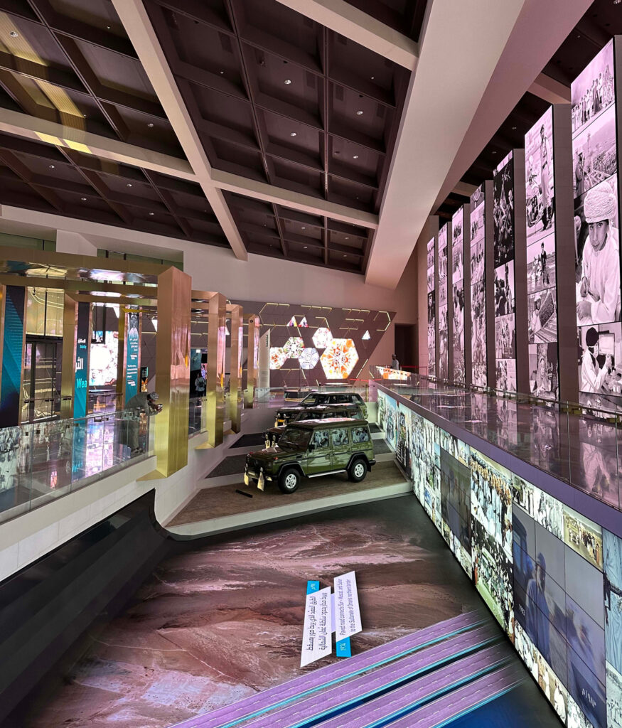 A large hall with hi tech display screens on the walls and floor as well as a collection of royal cars