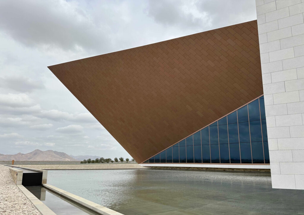 Geometric tower of Oman Across the Ages Museum rising into the sky above a reflection pool