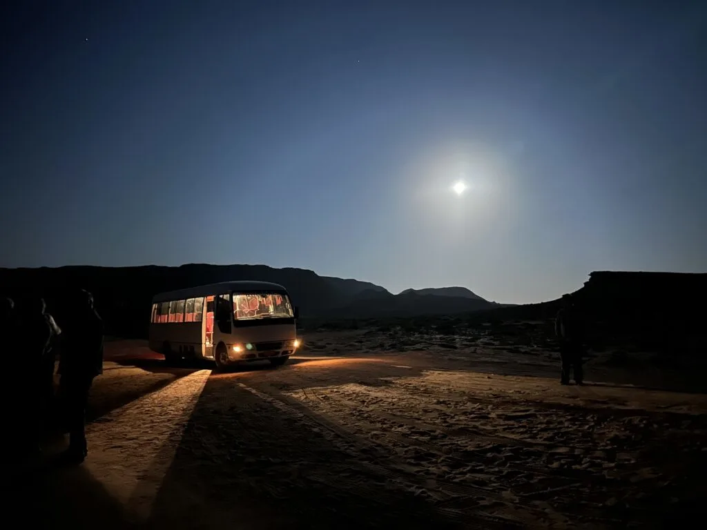 The bus at Ras Al Jinz Turtle Reserve visitor centre park near the beach at night. There is a full moon overhead
