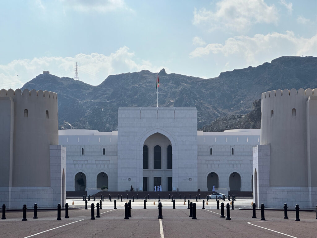 The front of Oman National Museum - a white building wit mountains behind it