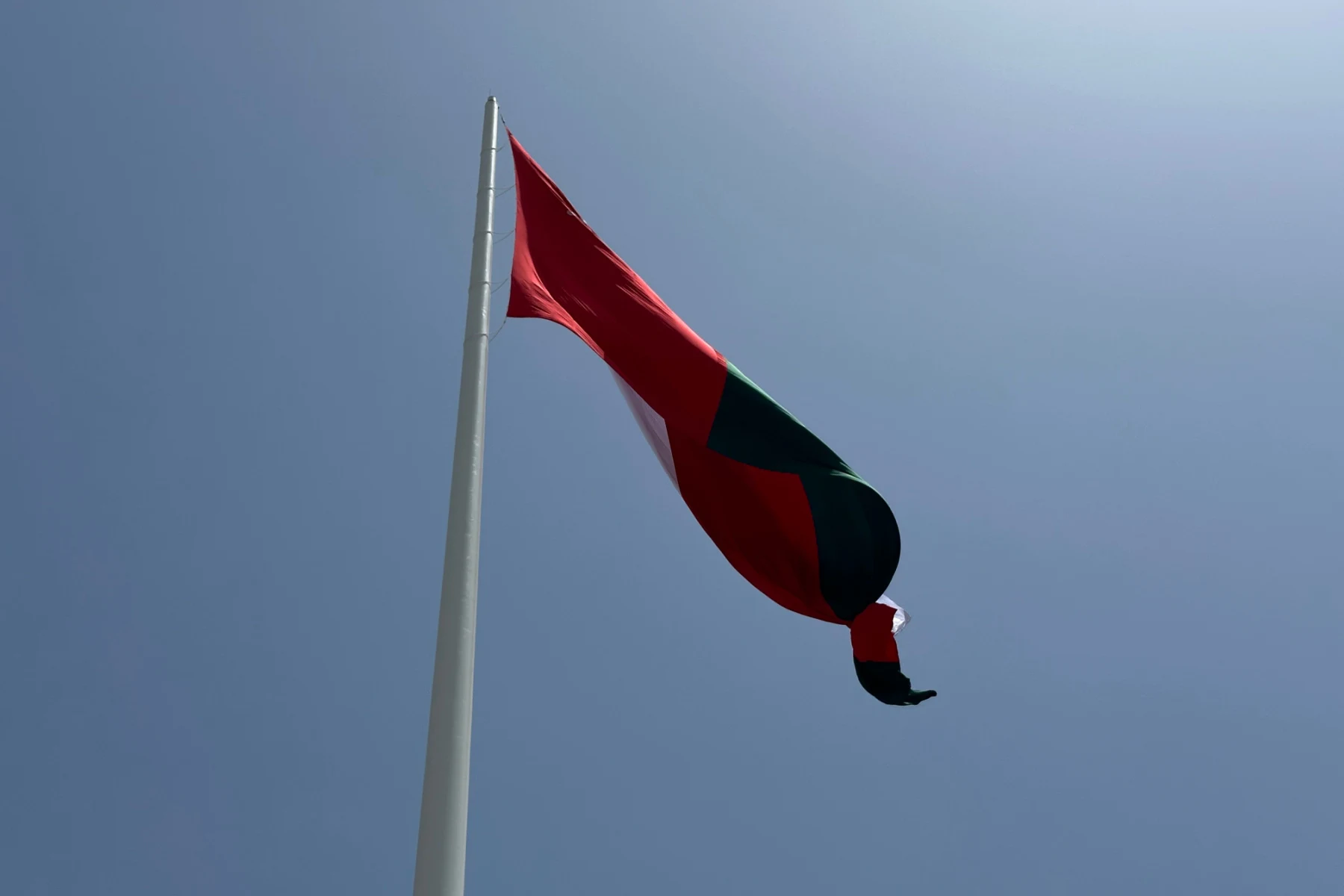The 18 metre by 31.5 metre Omani flag flying at the to of the flagpole in Al Khuwair Plaza against a blue sky