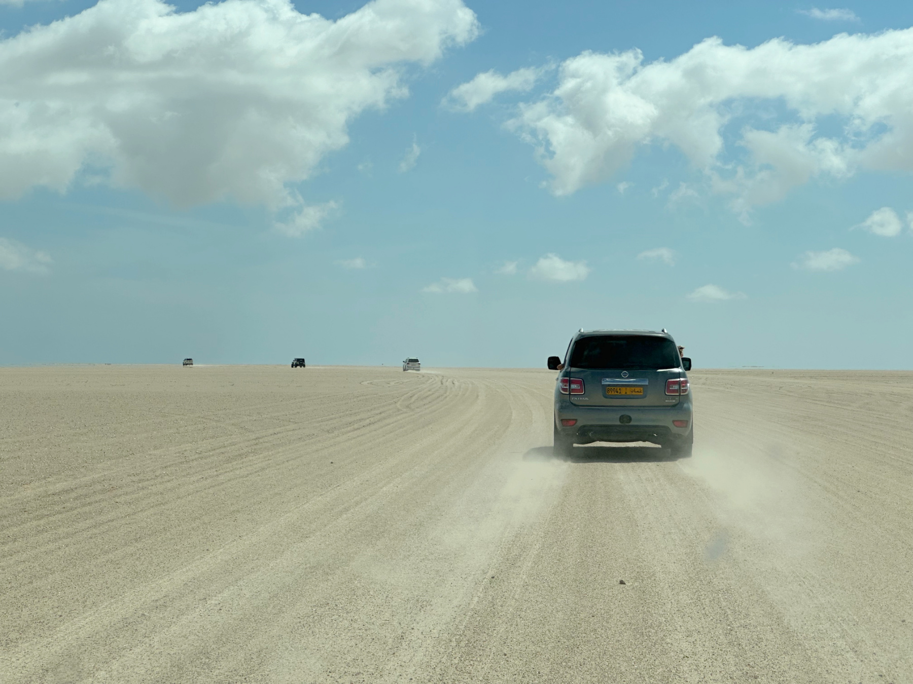Four spaced out 4x4 vehicles drive through the dry salt flats of Barr Al Hikman