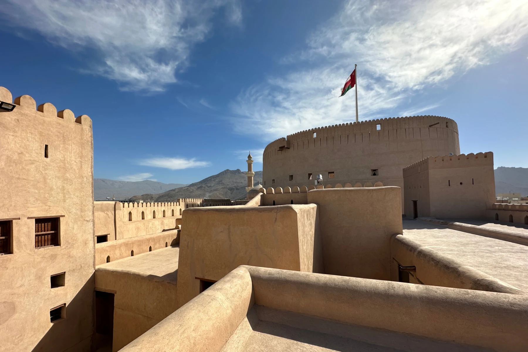 The roof of Nizwa Castle with the round have of Nizwa Fort. The Omani flag is flying inside the fort
