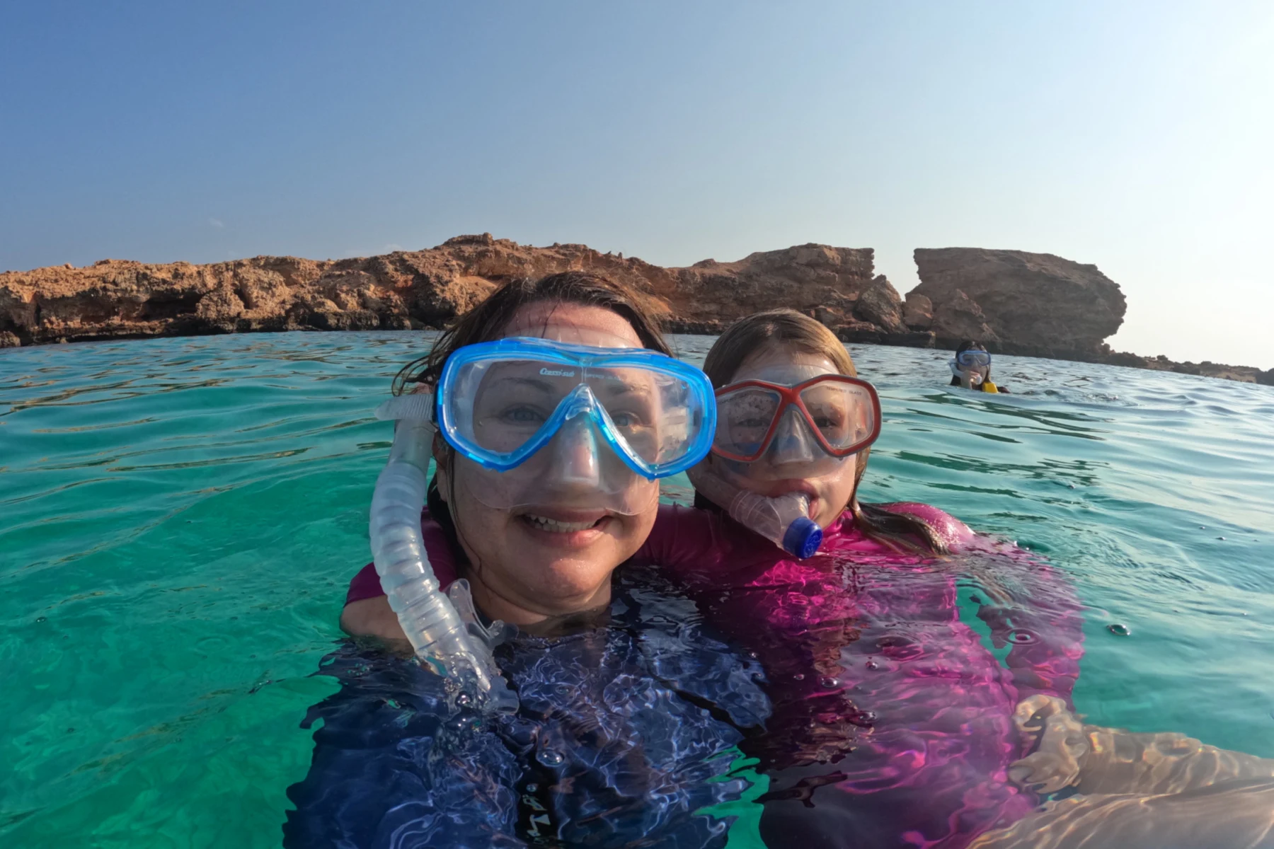 My daughter and I are on the surface of the water wearing snorkelling masks. Behind us is one of the Daymaniat Islands