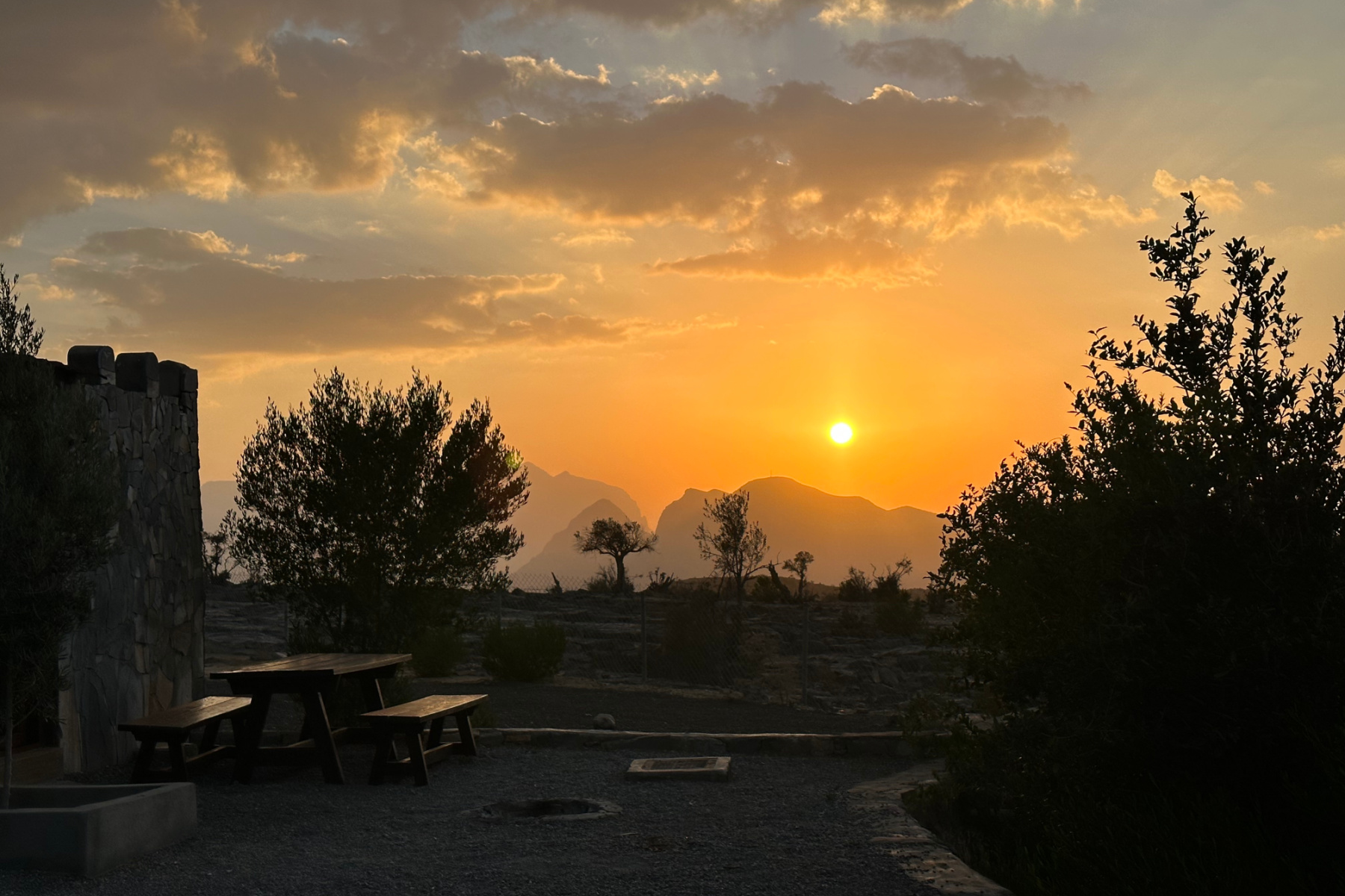 The sunset over the Hajar Mountains from Jebel Shams Resort. There are bungalows and outdoor seating in the foreground