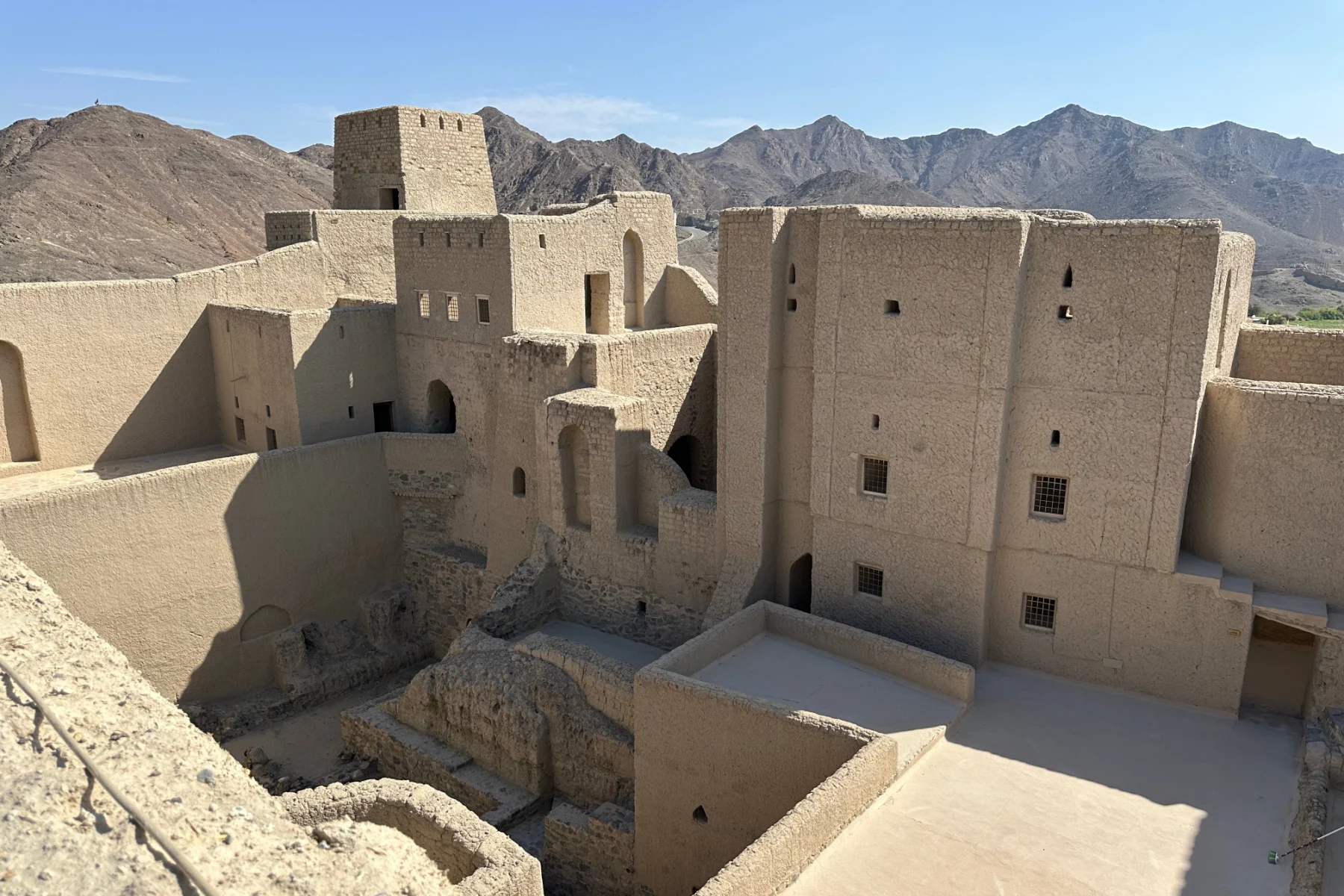 A view from the top of one of the towers in Bahla Fort. There is a collection of buildings that look like they have bee added to over years. In the background there are the tops of neighbouring mountains
