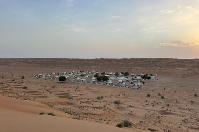 Sun setting over the dunes in Wahiba Sands desert. In the valley below is Desert Nights Resort