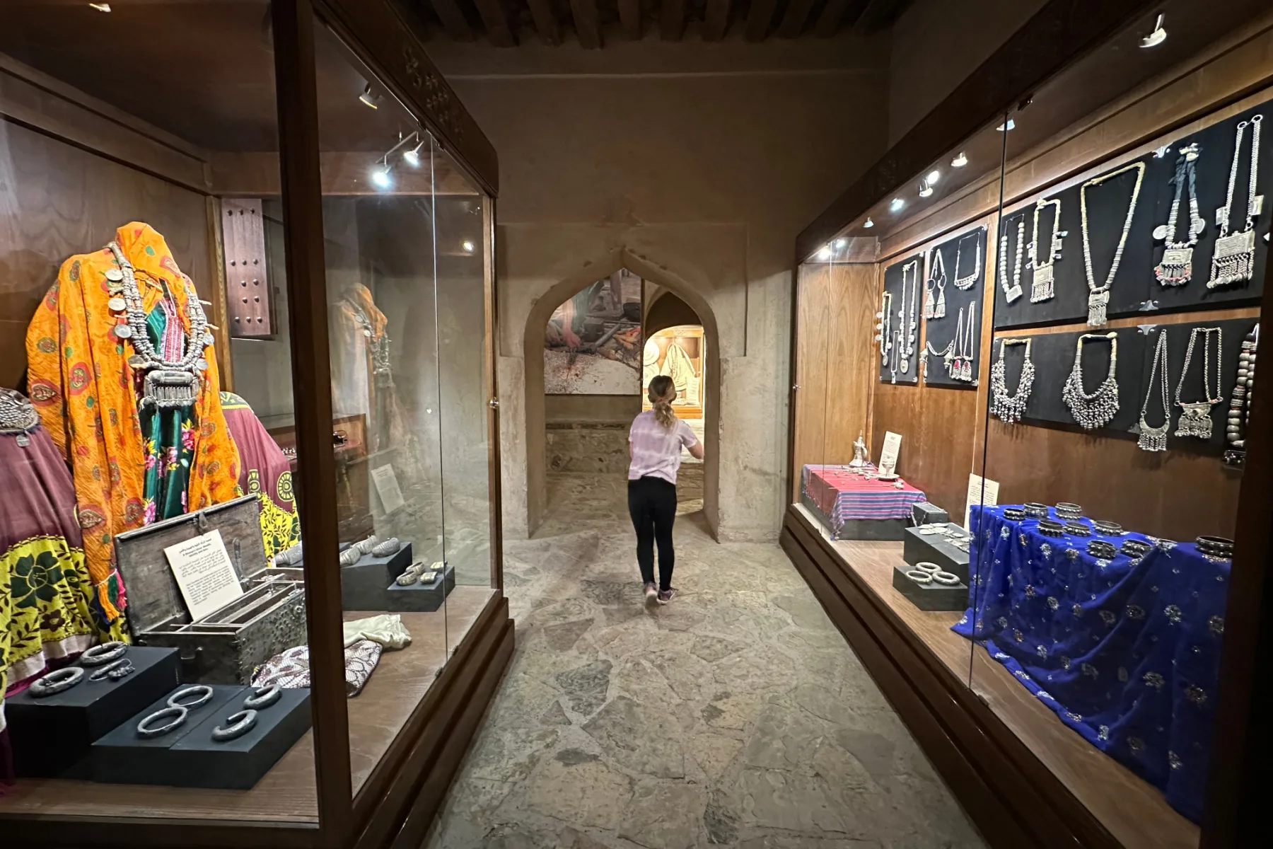My daughter walking between displays of Omani silver and items put into dowry boxes in Nizwa Fort