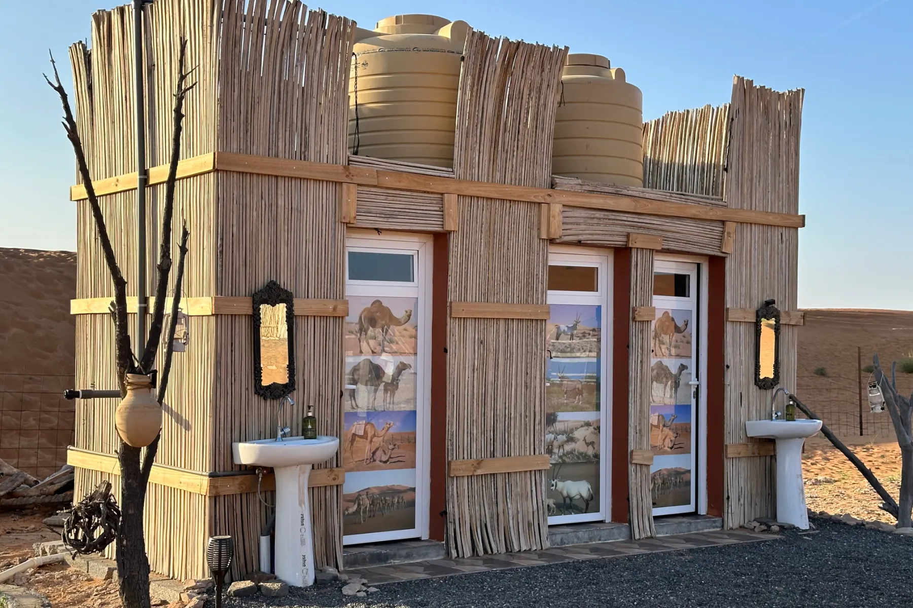 A close shot of the bathrooms at this Wahiba Sands camp. There are sinks outside and three doors into shower rooms with toilets