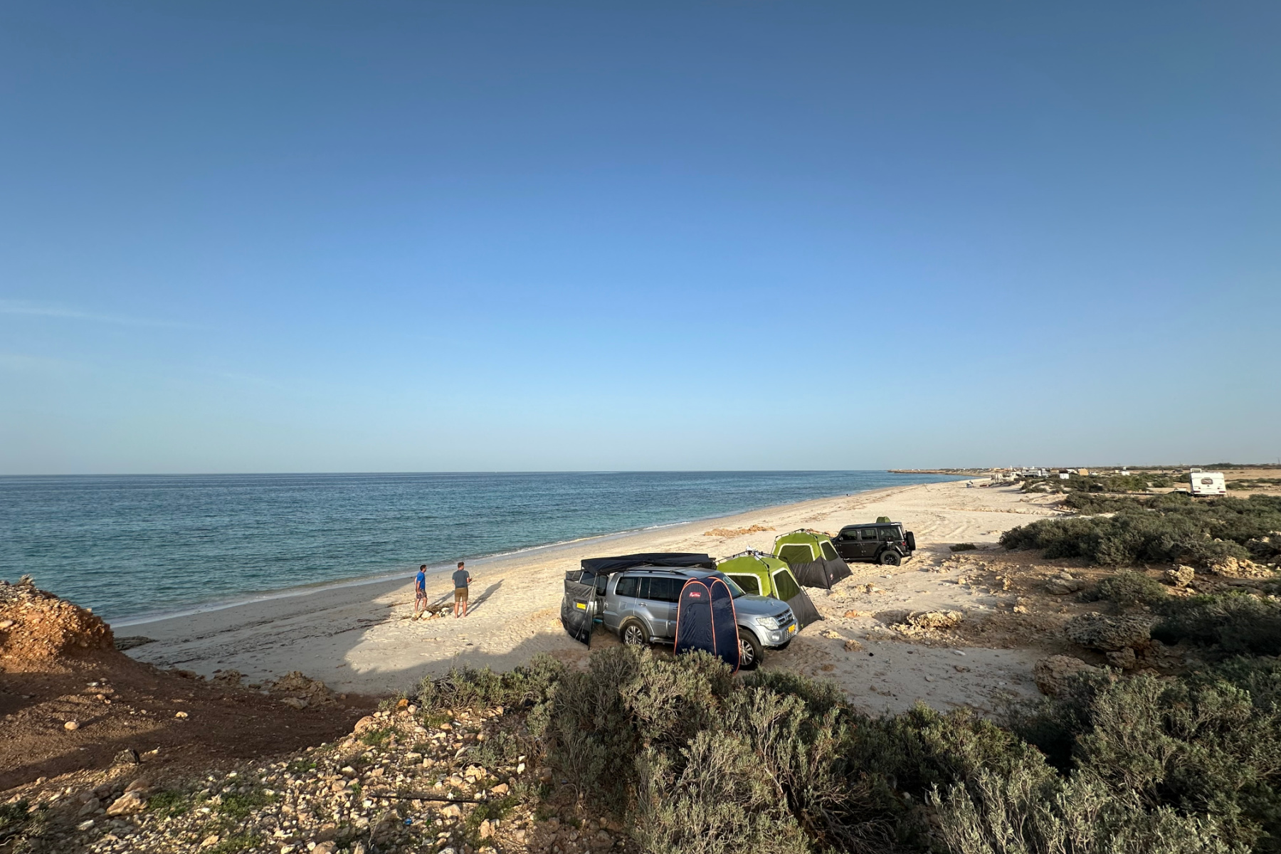 Camping with friends on white sands on the beach near Bimmah. The sea is blue and turquoise and the beach stretches into the distance