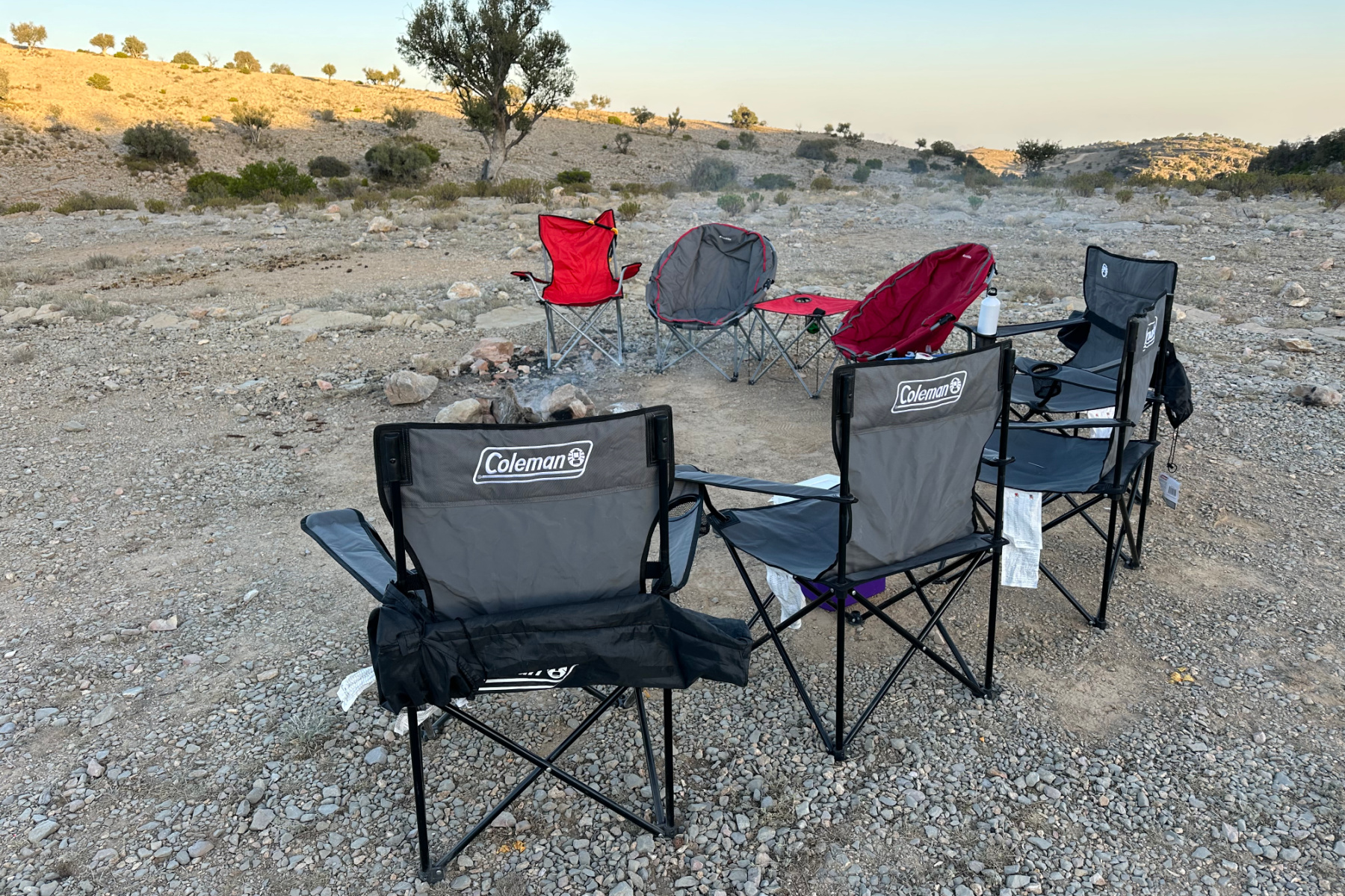 A collection of eight camping chairs set out around a campfire in a camping area on Jebel Akhdar