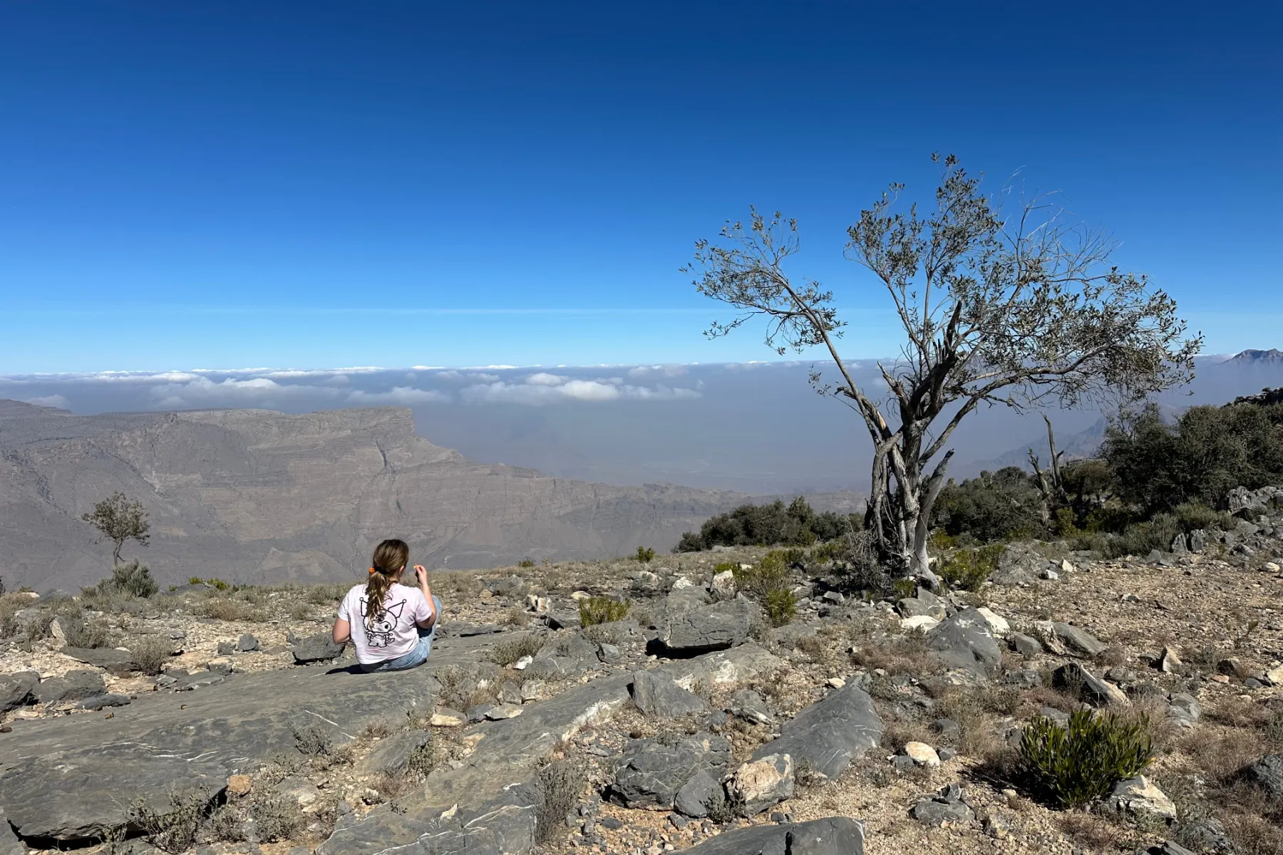 My daughter set on the ground at a view point on Jebel Akhdar. Below it's possible to see clouds rolling over the lower Hajar Mountains
