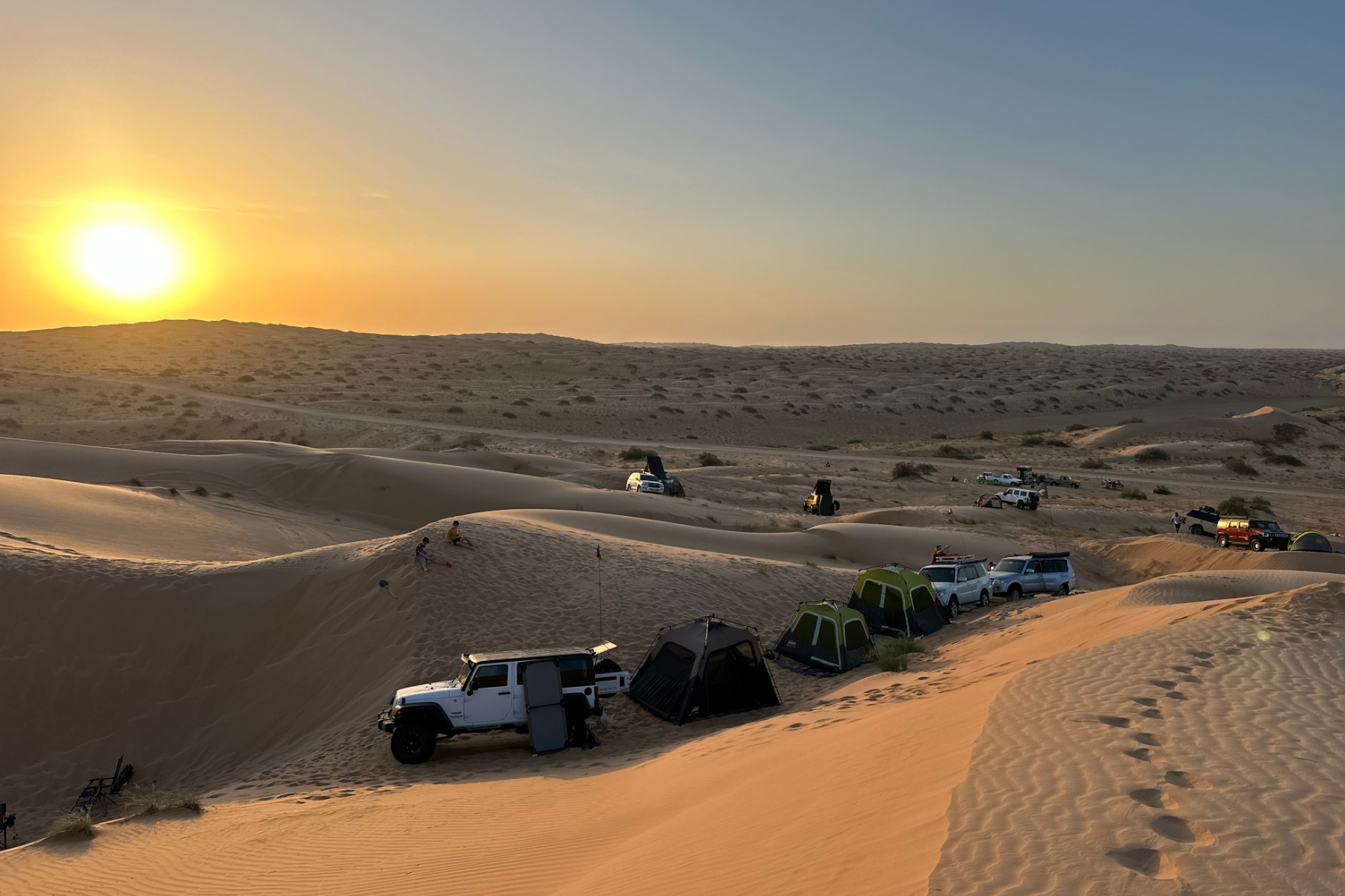 4x4 vehicles are parked in desert dunes at sunset