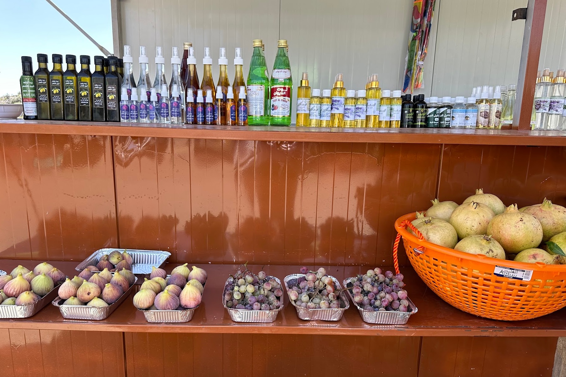 Rows of olive oil, scented water, honey and fruit on a market stall