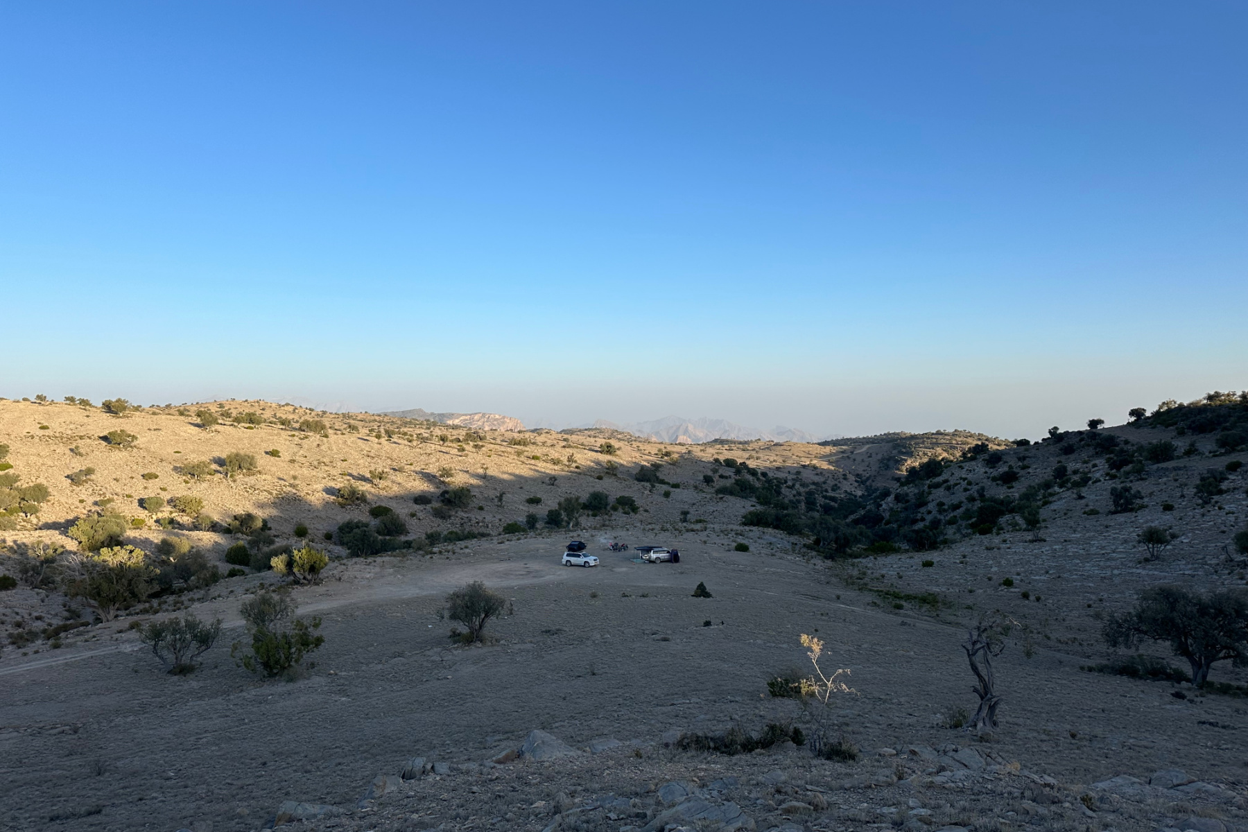 A view down to out camp with friends in a shallow valley on the plateau of Jebel Akhdar. The area is rocky and there are scrubby bushes around