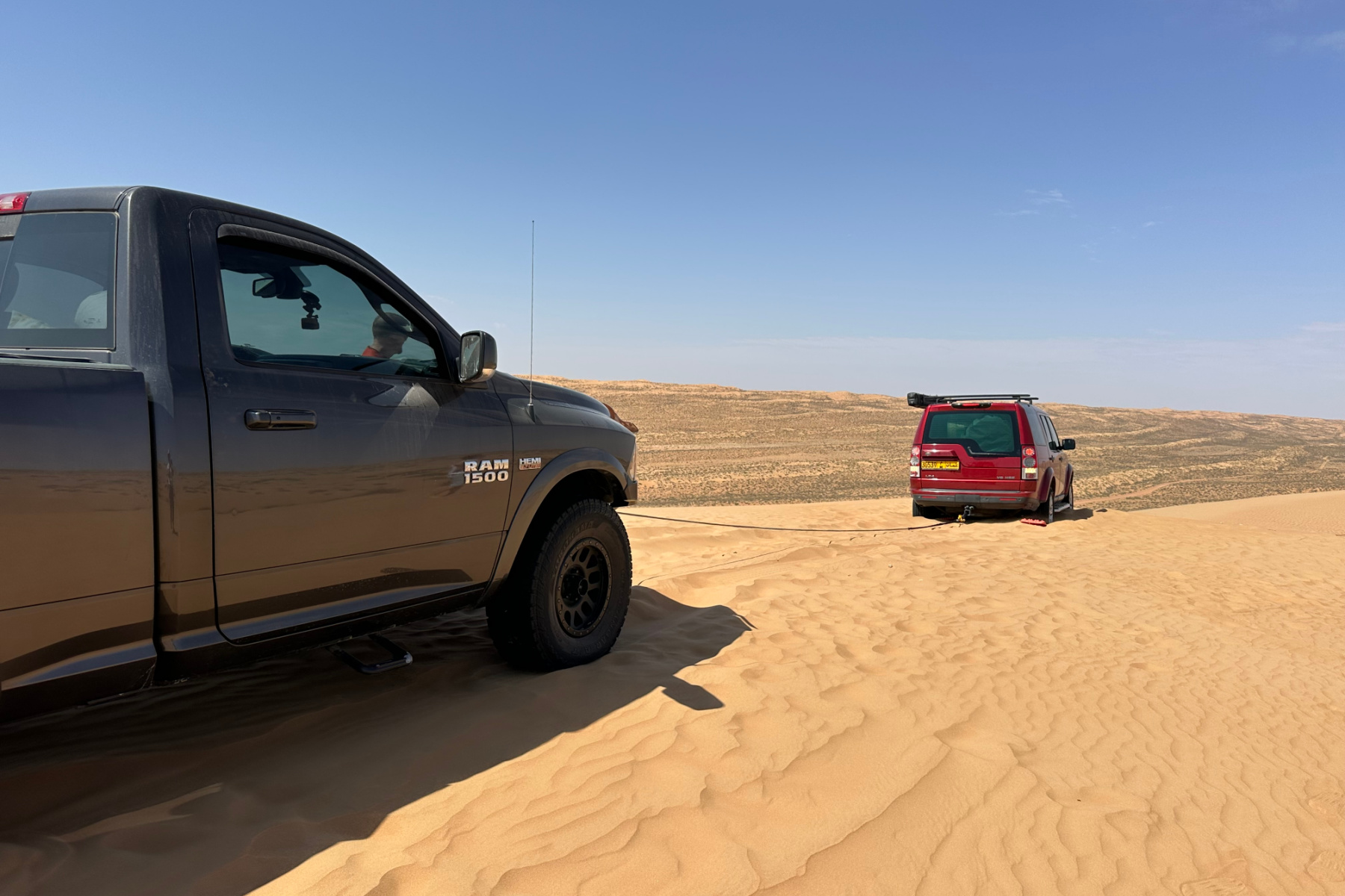 Our red car stuck in soft sand at the top of a dune. Our friends' truck is towing us out