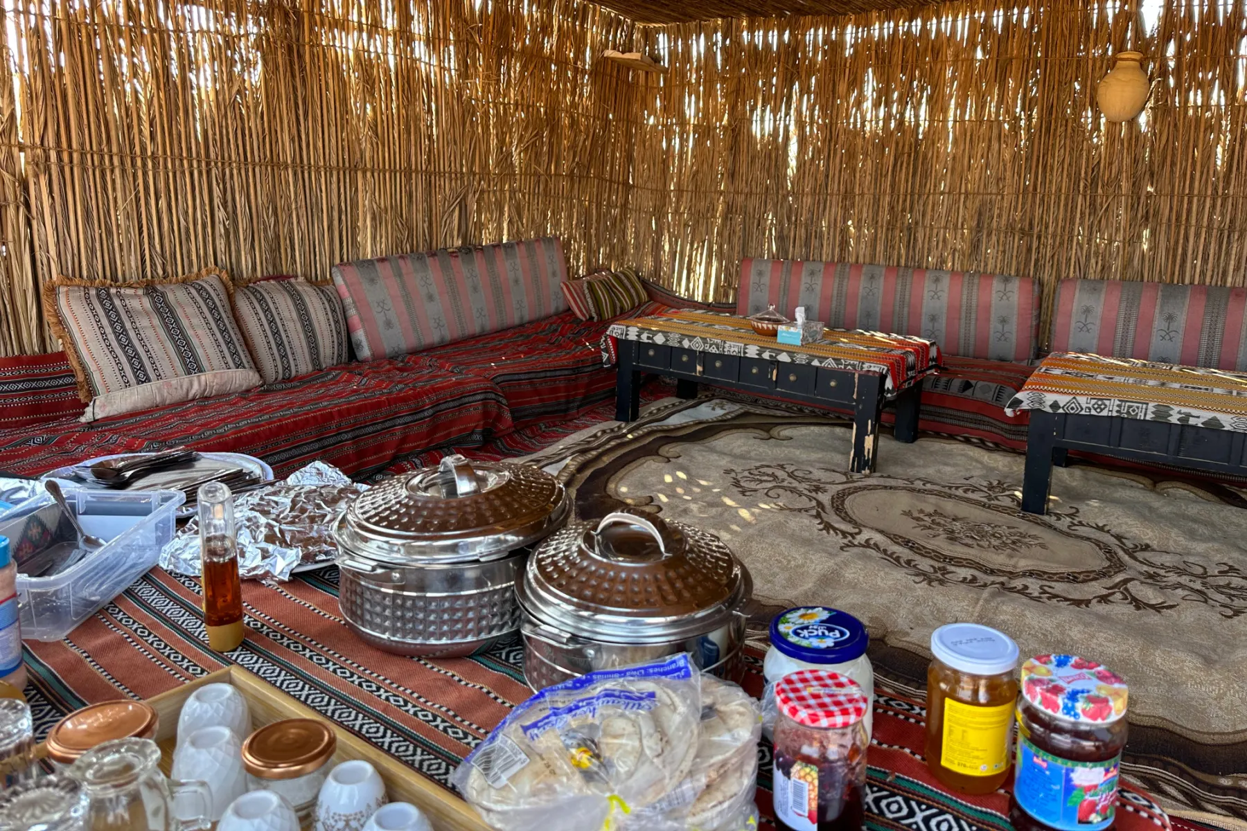 Inside the majlis at breakfast time. The table is laid with hot food containers, jam, honey and puck cheese