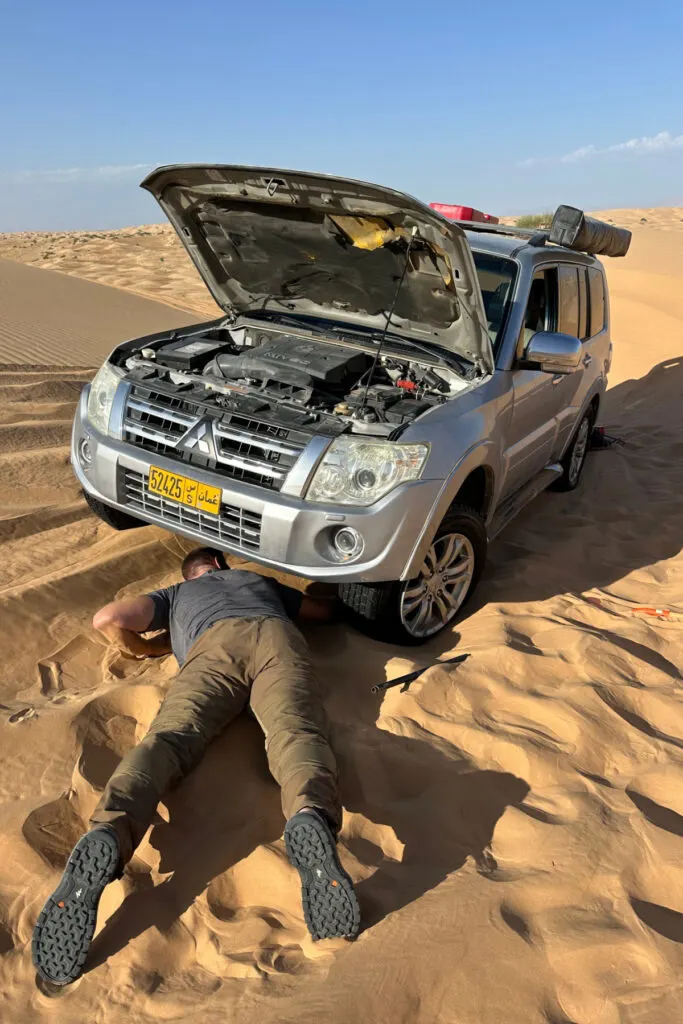 My husband laying under a 4x4 Pajero which has its bonnet up in the desert