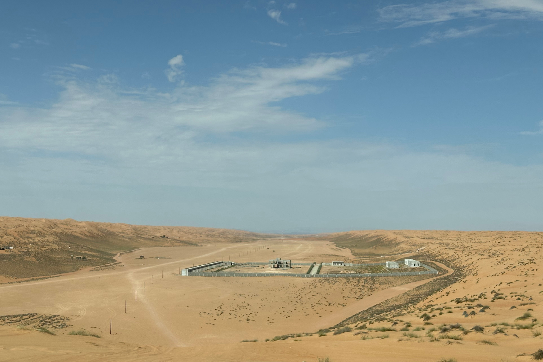 A view across a valley towards the end of our road trip. A desert camp is being constructed below and the Hajar mountains can be seen in the distance