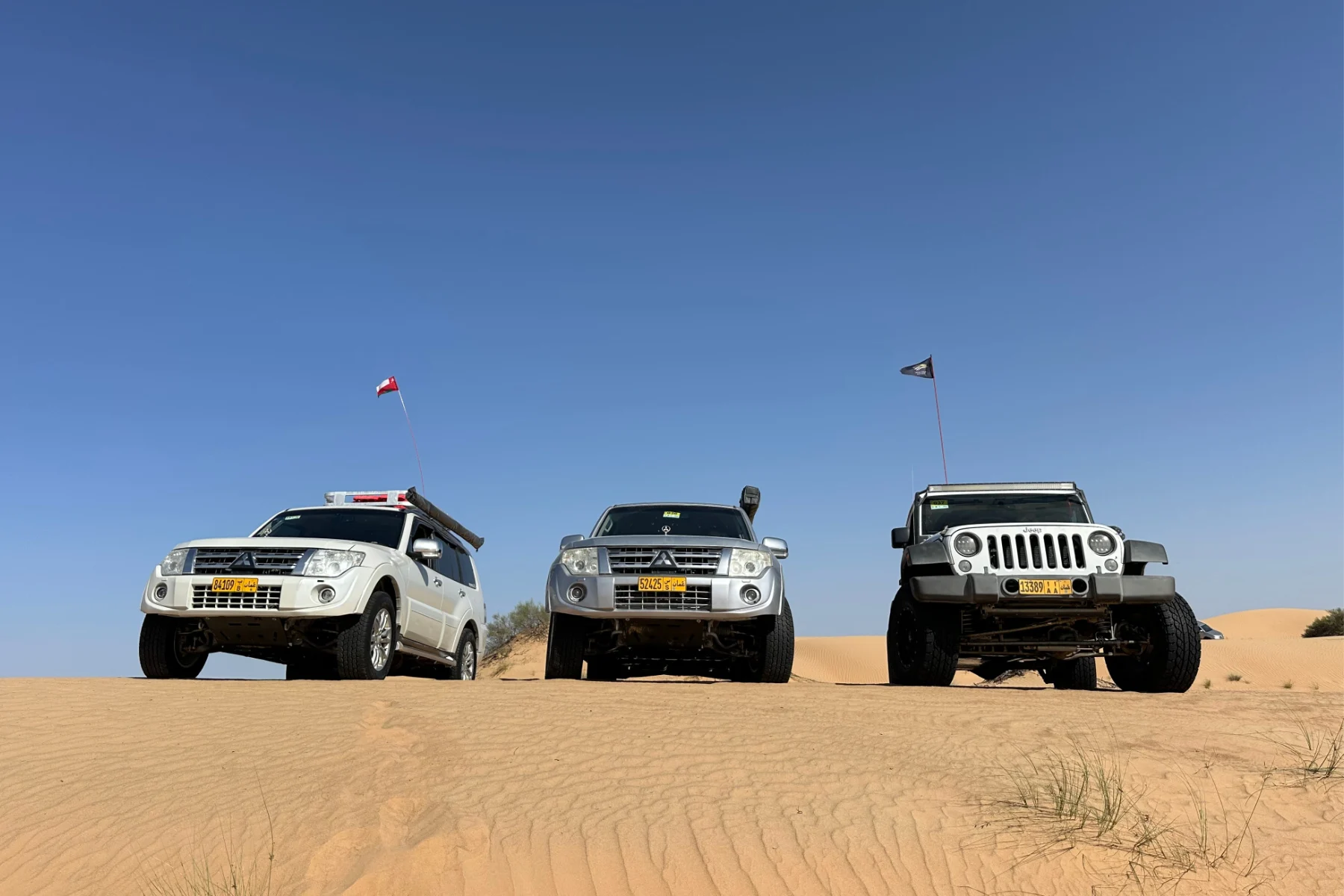 Three 4x4 vehicles lined up along the top of a sand dune
