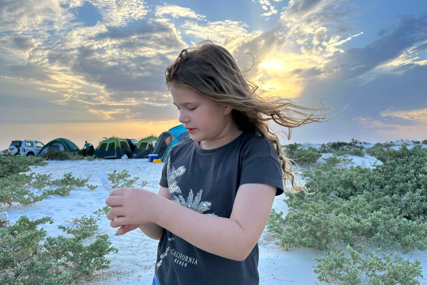 My daughter looking at the shell of a crab she has found on the beach at Bar Al Hikman. Our camp is set up in the background