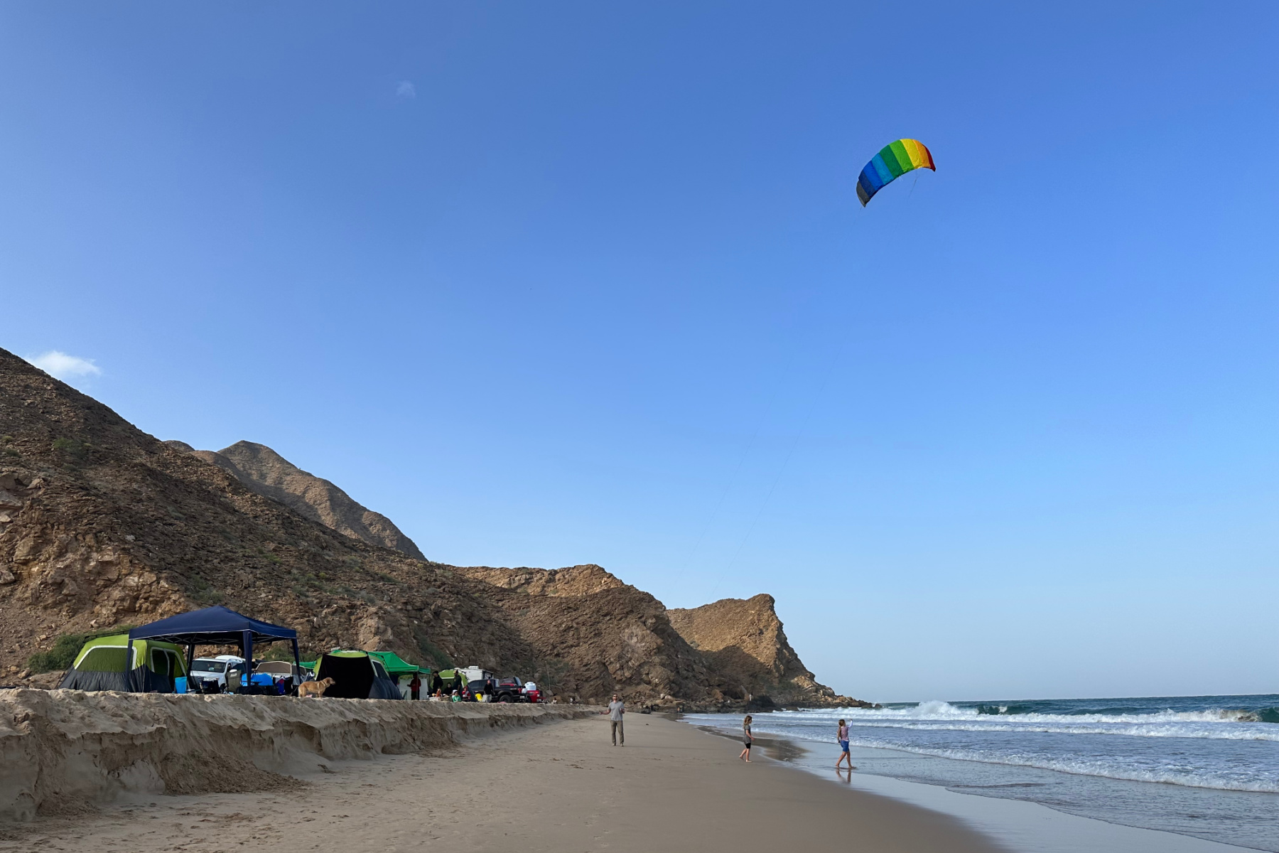 A view along the golden sands of Sifah Beach North towards my husband who is lying a kite. To the right is the sea and to the left are tend pitched along the beach