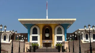The blue and gold front of Al Alam Royal Palace with the Omani flag flying above it