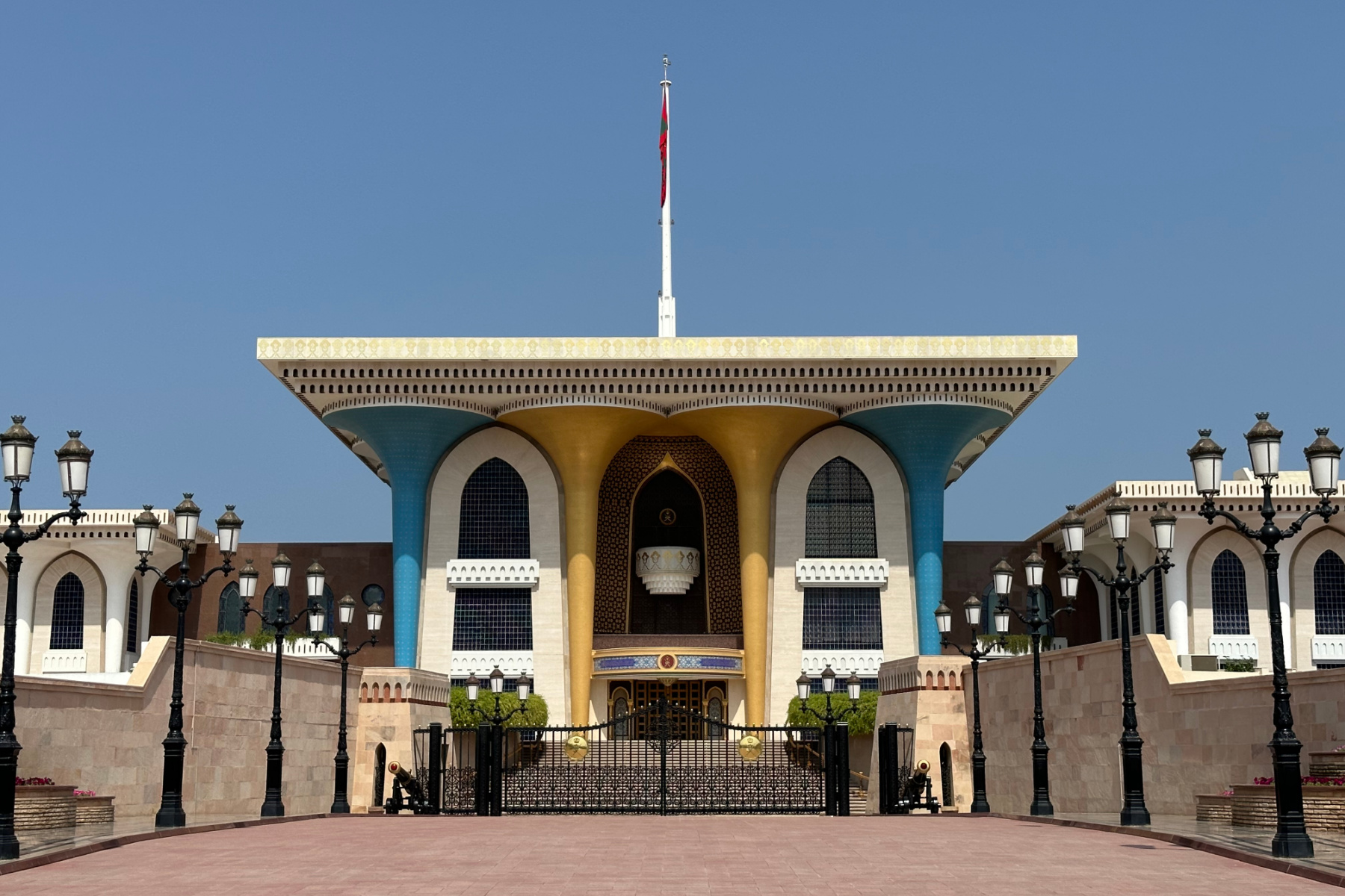 The blue and gold front of Al Alam Royal Palace with the Omani flag flying above it