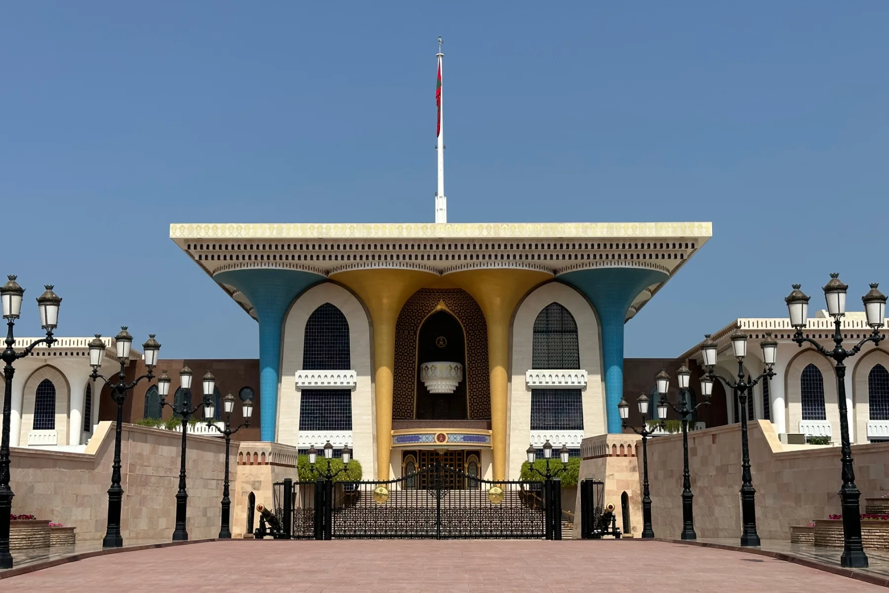 The blue and gold front of Al Alam Royal Palace with the Omani flag flying above it
