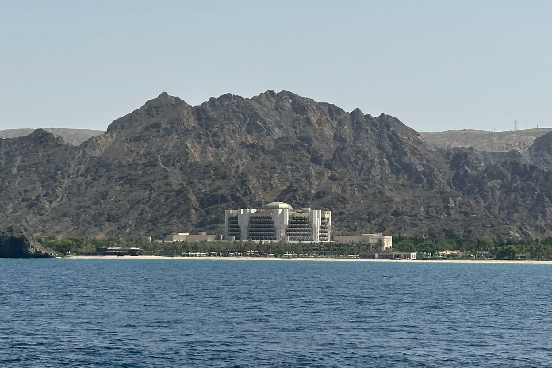 The Al Bustan Palace Ritz Carlton hotel seen from the sea with mountains rising behind it