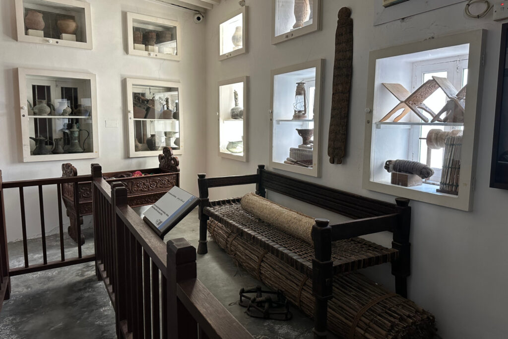 A vintage bench and cabinets of old pottery and household items in the Place and People Museum in Muttrah