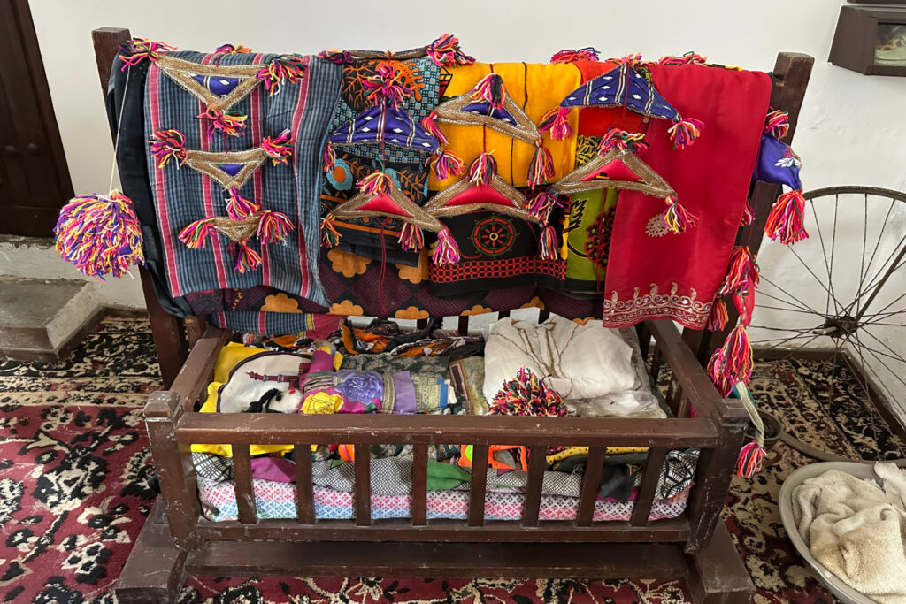 Colourful textiles and crafts draped over a wooden baby cot in the Place and People Museum