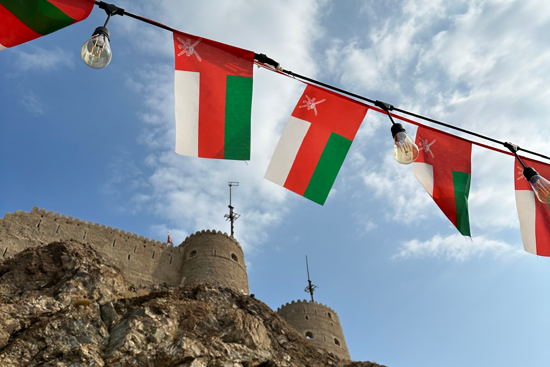 A string of Omani flags flies with the battlements of Muttrah Fort in the background