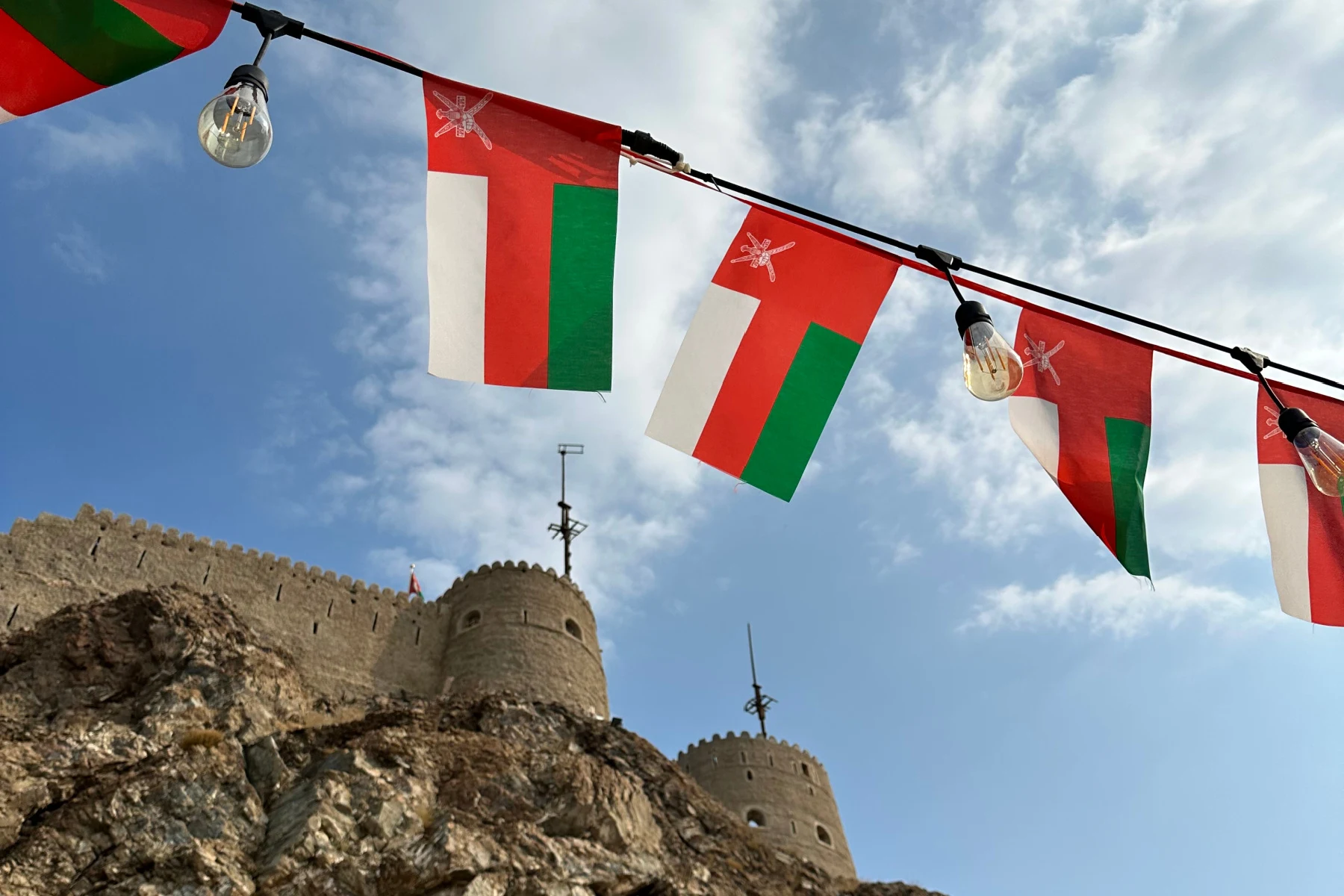 A string of Omani flags flies with the battlements of Muttrah Fort in the background