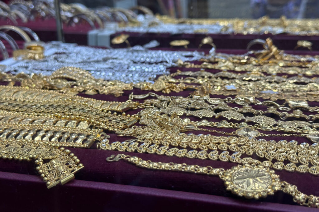 Rows of gold chains with silver chains in the background. They are displayed in a cabinet