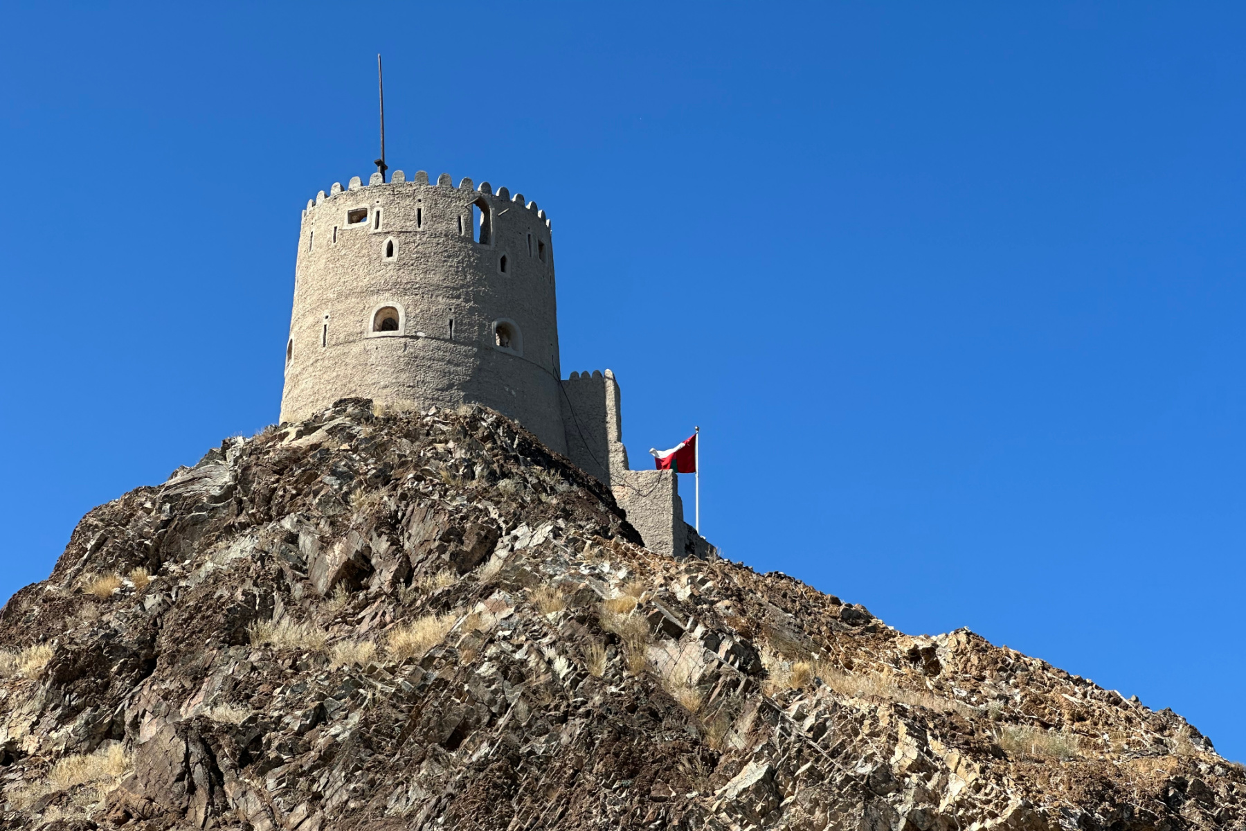 A view of one of Muttrah Fort's towers from below. The sky in the background is bright blue