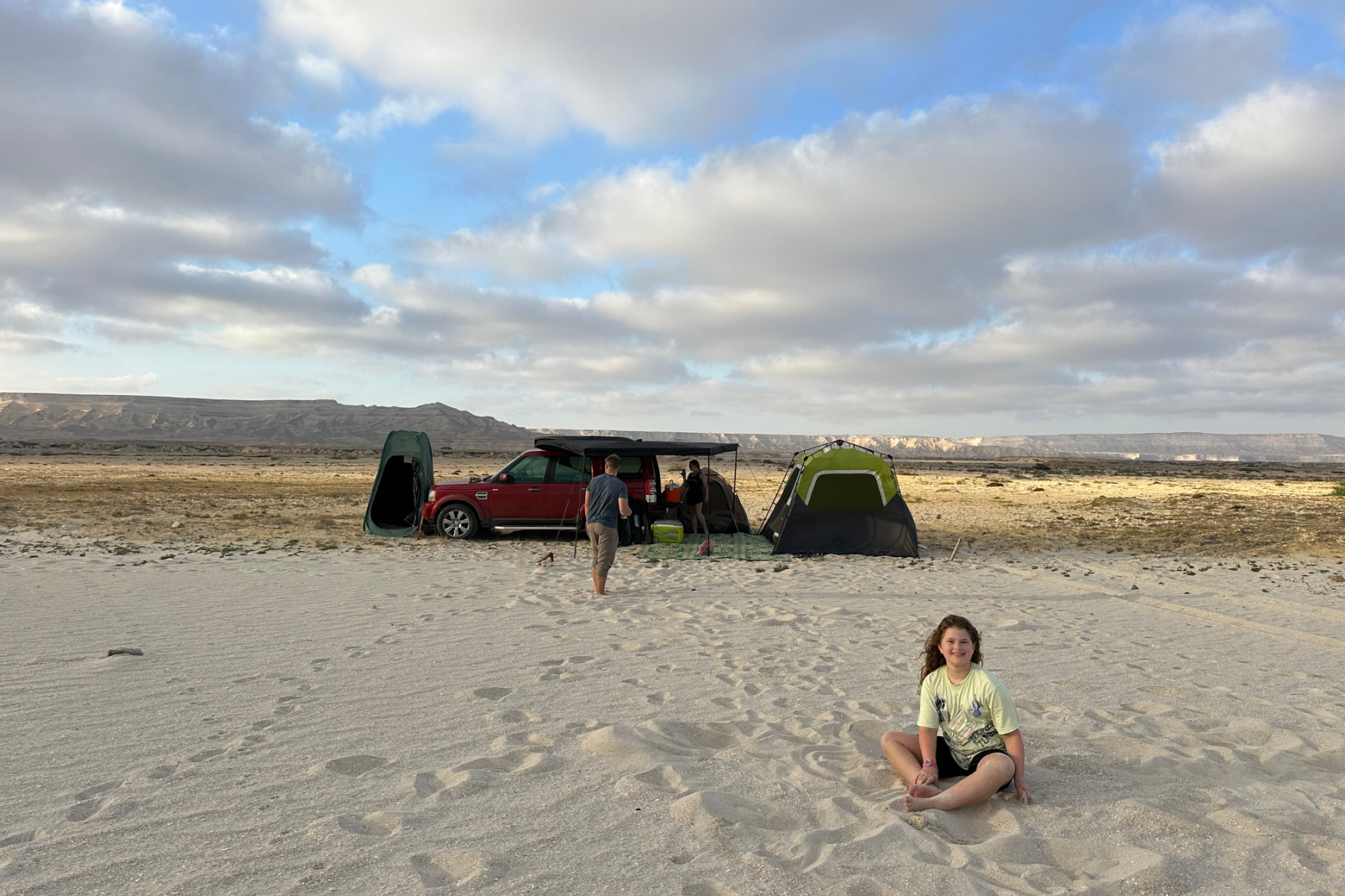 Our daughter playing in the sand on Ash Shuwaymiyyah beach with our tent and car in the background. In the distance are mountains